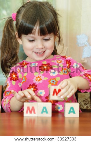 The girl and toy cubes. The child collecting a word mama from cubes.