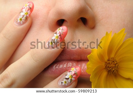 Female face close up c flower in a mouth and nail art. Figure of camomiles on nails