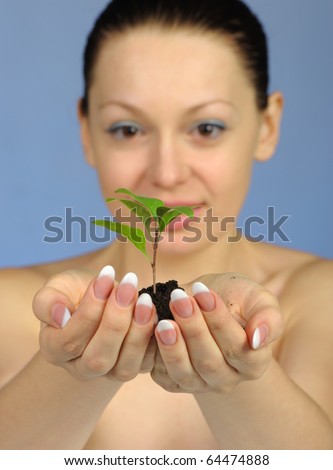 The woman holds in hands soil with a plant. Selective focus. A blue background