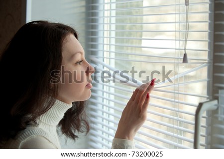 Expectation. The young girl looks out of the window through a jalousie