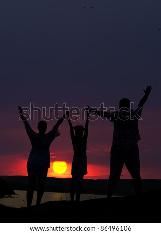 The family from three persons welcomes the sunset sun.