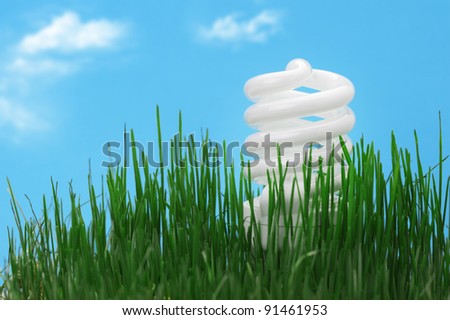 Energy saving compact fluorescent lightbulb in a green grass and cloud sky
