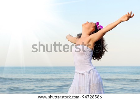 The woman in a white sundress on seacoast with open hands. Sun light