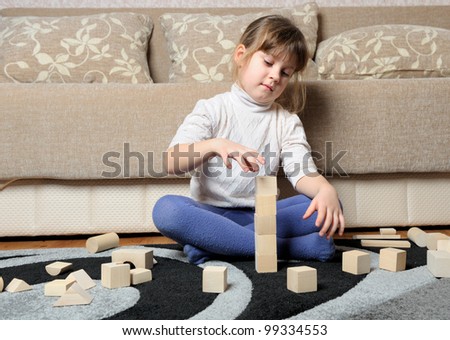 The little girl plays wooden toy cubes. A house room