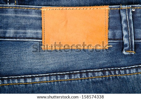 Highly detailed closeup of blank grungy leather label on worn blue denim with orange seams, good for background