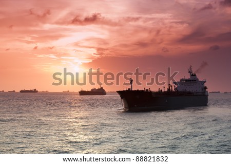 Merchant ships in silhouette backlit by the sun set