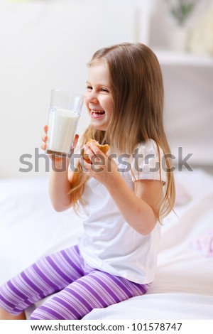 Happy child drinking milk with croissant in bed