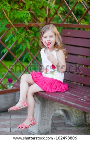 Joyful fashionable kid eating big heart lollipop in the summeer park
