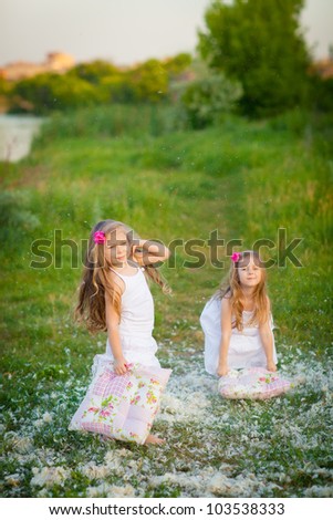 Happy childhood: Adorable little girls having fun with pillows outdoor