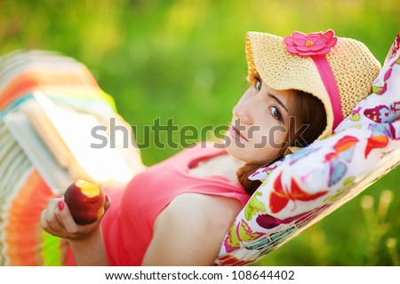 Young woman lying in a hammock in garden and reading a book and eating peach