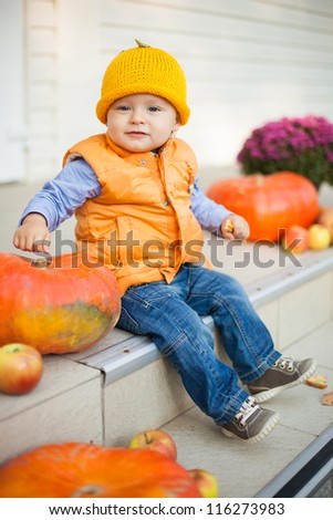 Adorable  child sitting on house porch near pumpkins