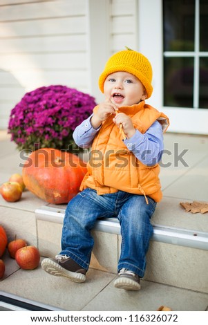 Cute child sitting on house porch near pumpkins