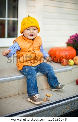 Happy little child sitting with  on house porch on halloween