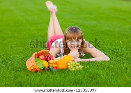 Young sportive woman lying on a grass with basket of fruits and vegetables