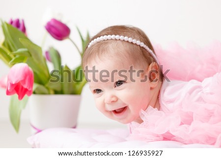 Cute young  smiling infant girl in a pink petty with bouquet of tulips