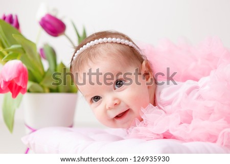 Cute young  infant girl in a pink petty with bouquet of tulips