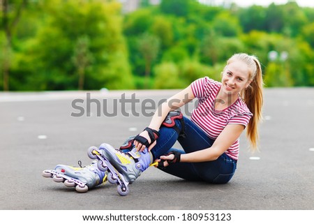 Woman skating in park. Girl going rollerblading sitting in grass putting on inline skates