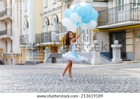 Adorable girl with blue and white balloons on the city street