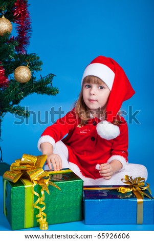 Pretty baby miss Santa sitting near  Christmas tree and gifts