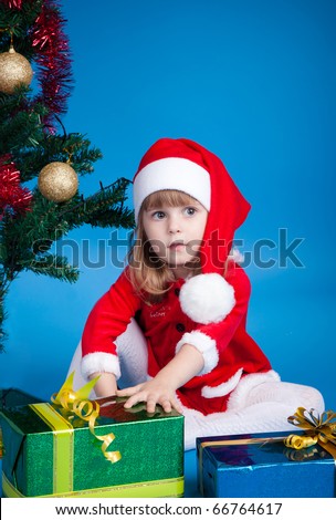 Little kid in Santa costume sitting at Christmas tree