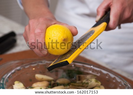 Gourmet chef grating a lemon, adding zest to potatoes