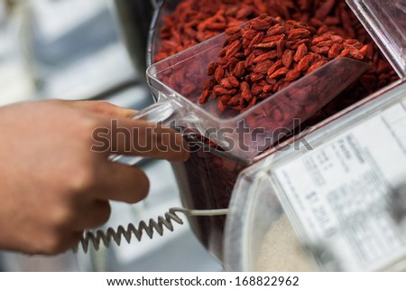 woman scooping Goji berries from the bulk food dispenser at an organic grocery store