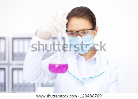 Young female researcher observing liquid in flask