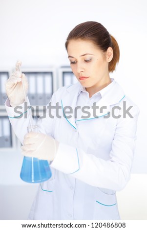 Young chemical female researcher with vials and flasks makes some experiments in laboratory