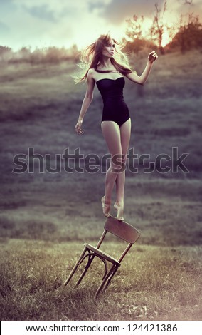 beautiful girl balances on back of chair outdoors. Artwork
