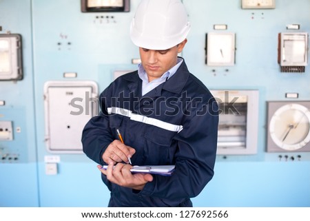 Portrait of young smiling engineer taking notes in control room