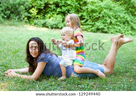 Portrait of a young mother lying on the lawn with her children sitting on her back, in the outdoors.