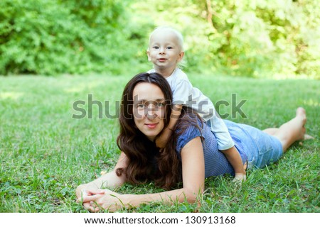 Portrait of a mother lying on the lawn with her son sitting on her back, in the outdoors.
