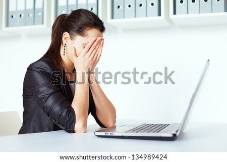 Portrait of tired young business woman covering his face by hands with laptop at the office