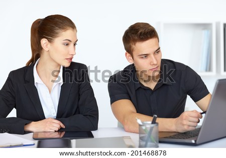 Two beautiful young businesspeople sitting at table in office and looking at laptop computer screen