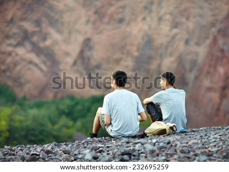 Two tourist young men sitting on rocky cliff and enjoying beautiful view
