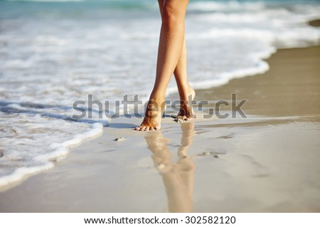 Closeup detail of woman legs and feet walking on the sand of the beach with the sea water in the background. Vacation holiday concept