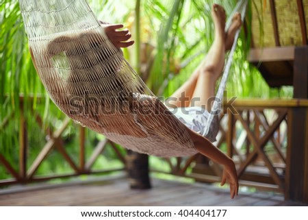 Young beautiful woman relaxing in hammock in a tropical resort.back view