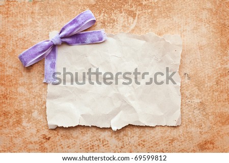 ripped piece of paper with purple bow on grunge paper background. vintage retro card