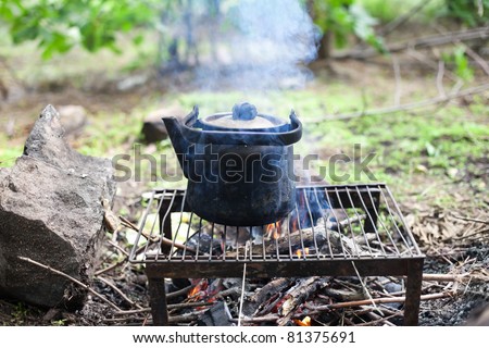 black old smoked teapot on the campfire on picnic in wood in the summer