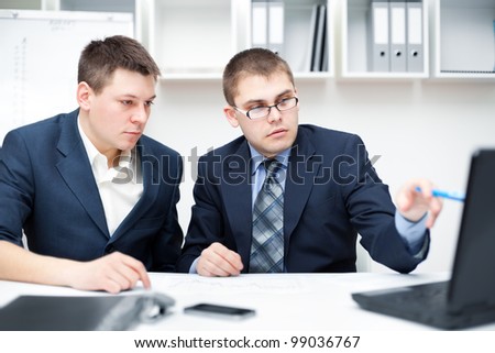 Two young businessmen working together with computer at office desk