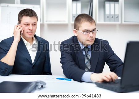 Two young businessmen working together with laptop at office desk, looking at screen