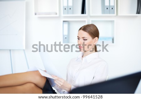 Portrait of a beautiful young smiling business woman doing some paperwork with legs on desk at office in bright office