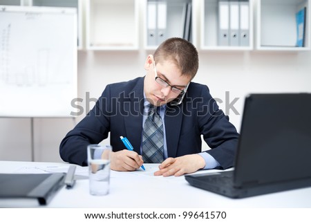 Portrait of young business man in the office doing some paperwork and talking on cell phone