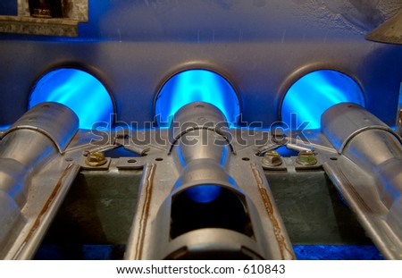 Closeup of inside a home natural gas furnace showing blue jets of  fossil fuel burning.