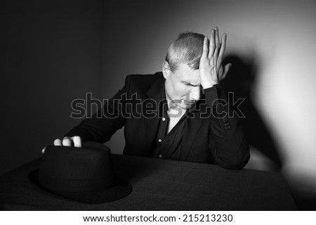 Man in black hat at the age of forty-six years old puts his hand on his hat and puts his hand to his forehead   on the background of a rough wall with texture