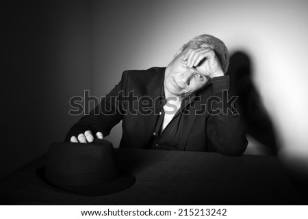 Man with  black hat at the age of forty-six years old put his hand on his hat and  hand covers one eye looking at the camera on the background of a rough wall with texture