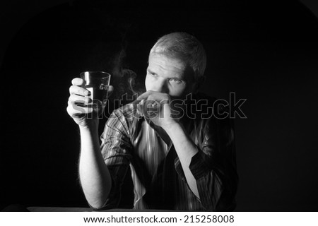 Man in a striped shirt at the age of forty-six years old holding a glass in his hand and smokes on the black background