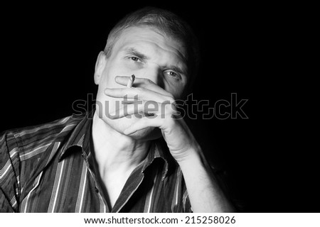 Man in a striped shirt at the age of forty-six years old smoking and looking at the camera on the black background