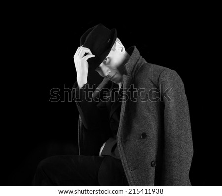 Man in black hat amd coat at the age of forty-six years old put his hand on his hat looking at the camera  on black  background