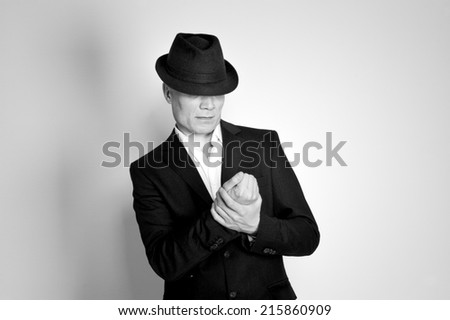 Man in suit and black hat at the age of forty-six years old looking at his hands on the background of a rough wall with texture
